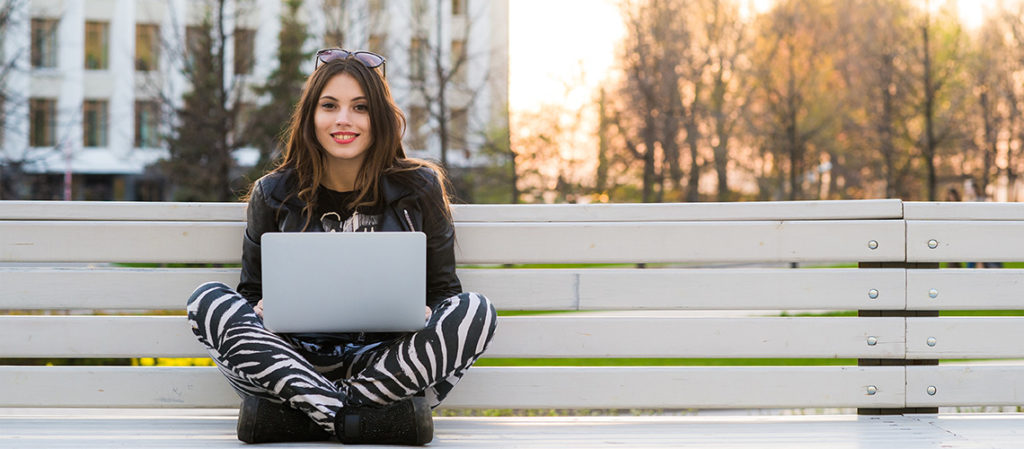 Female college student sitting on a bench with a laptop computer